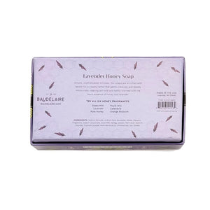 The BAUDELAIRE - LAVENDER HONEY SOAP 3.5 OZ, 2 BAR GIFT BOX features two hexagonal, triple-milled soaps with a beehive design, nestled in a decorative purple floral box and partially opened to reveal the lavender-colored bars inside.