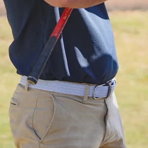 The ROOSTAS - SARASOTA WOVEN STRETCH BELT by ROOSTAS features sky blue and white weaving, brown leather ends, and a silver buckle, shown coiled with the buckle at the front.