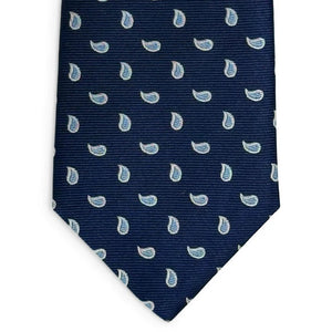 A rolled-up PETER-BLAIR - CAPE COD SILK TIE IN NAVY AND BLUE by BIRD DOG BAY, handmade in New York, featuring a navy blue silk fabric with a repeating light blue and white paisley pattern, displayed on a white background.