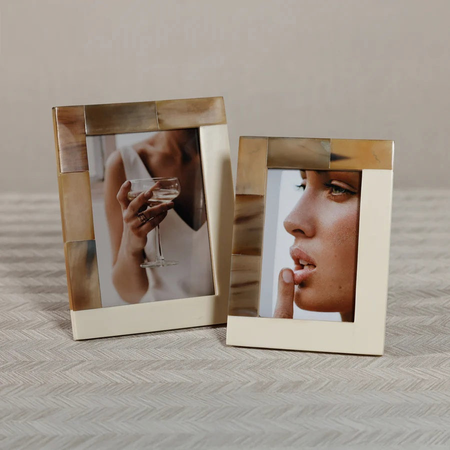 A woman in a white top, holding a glass of white wine or champagne with her face obscured, is displayed in the ZODAX WHITE HORN AND IVORY RESIN FRAME - 5X7, which features an elegant neutral-toned border.
