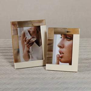 Close-up of the corner of the ZODAX WHITE HORN AND IVORY RESIN FRAME (4x6), elegantly crafted in soft beige tones. The frame displays a photo featuring hands holding a vintage camera, with the person's face partially out of view to emphasize the camera and hands.
