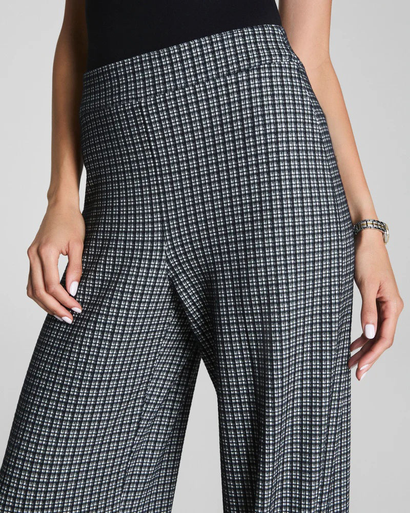 A person wearing SPANX Ponte Wide Leg Pant in Mini Collier, paired with a black top and black pointed shoes, stands with their back slightly turned.