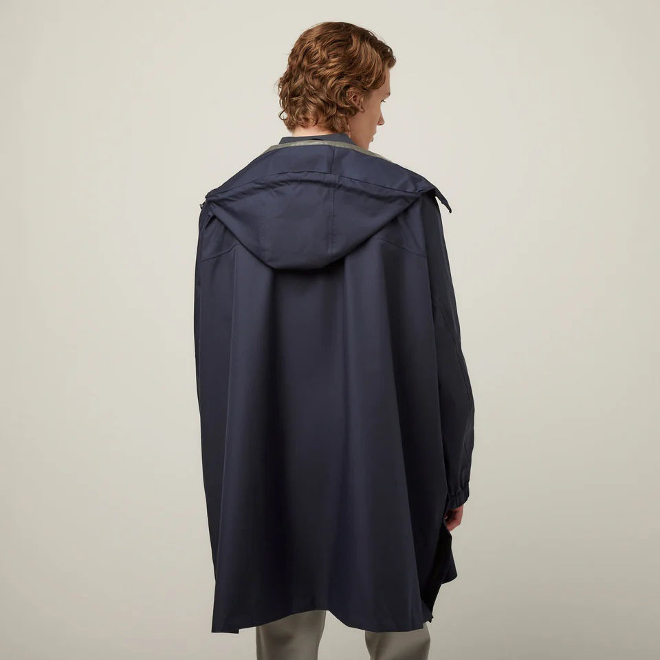 A person with short, wavy hair is seen from behind wearing the TILLEY - PACKABLE HOODED PONCHO by TILLEY in dark navy, featuring a hood and a loose, water-repellent fit, set against a plain light background.