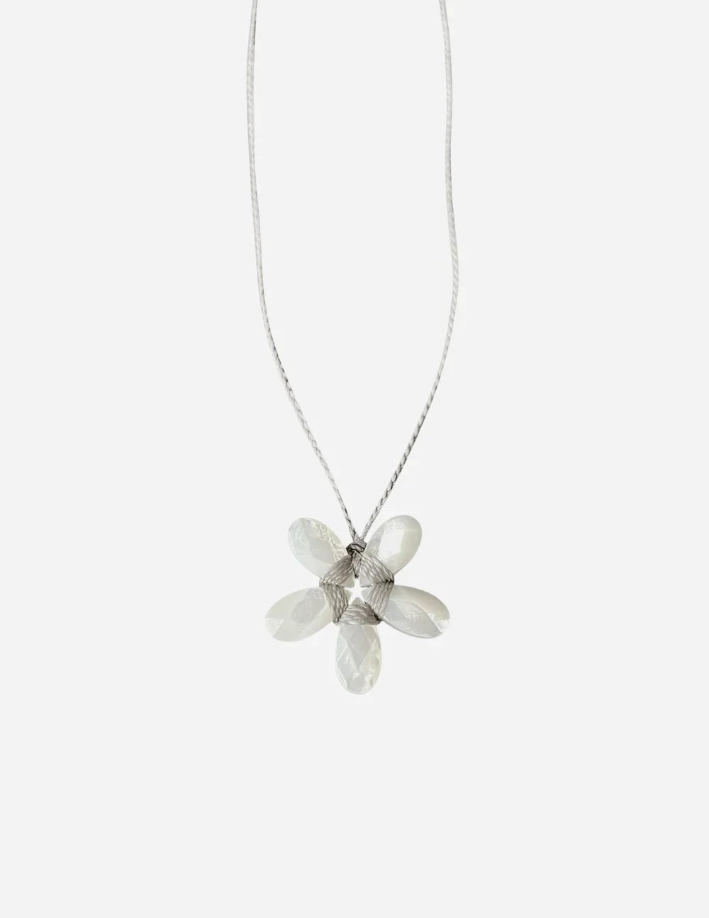 A white mannequin is dressed in a curly beige faux fur coat and adorned with the ANN LIGHTFOOT - SMALL MOTHER OF PEARL FACETED FLOWER NECKLACE by ANN LIGHTFOOT. The softly blurred background features light-colored walls and window blinds.