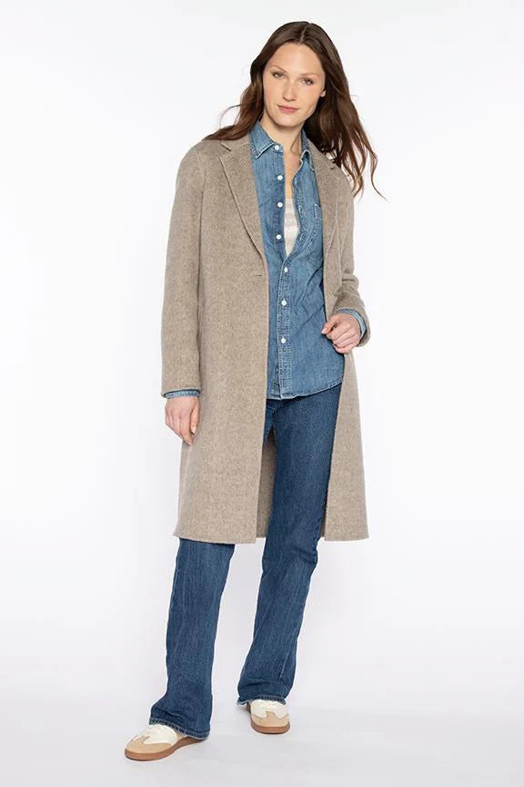 A woman with long brown hair and a confident expression stands against a white background wearing the KINROSS CASHMERE Brushed Herringbone Notch Collar Coat over a denim shirt and jeans, paired with white and beige shoes.