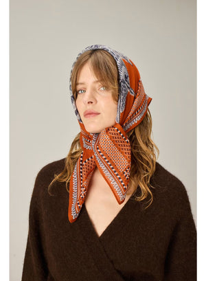Showcasing a drawing of a striped cat and an intricately detailed owl perched side by side on a branch, set against a terracotta brown background with an ornate patterned border, the INOUI EDITIONS - CHOUETTE SQUARE MODAL SILK SCARF IN TERRACOTTA by INOUI is expertly crafted in India. Measuring 70 x 70 cm, this unique scarf features intricate details reminiscent of traditional artistry.
