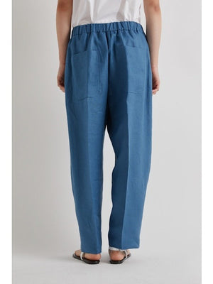 A person stands against a plain light background, cropped at the shoulders, wearing MEIMEIJ Pull On Barrel Pant in Cerulean with an elastic waistband, paired with a white shirt and sandals.