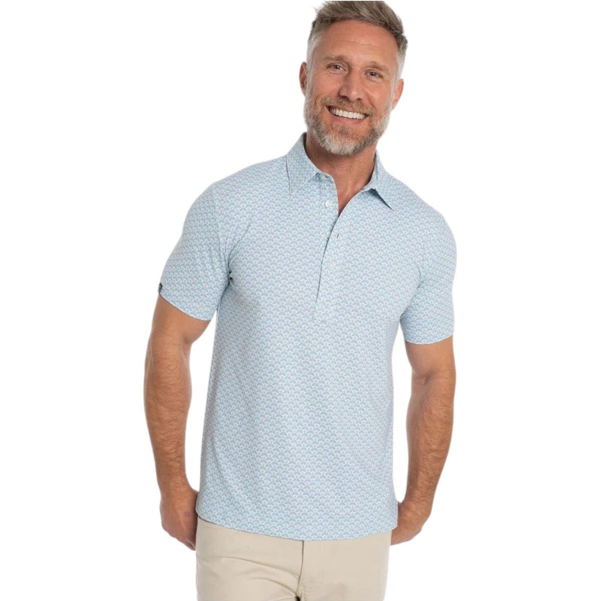 A smiling man with short hair and a beard wears the CRIQUET Performance Sport Range Polo in Trellis Print Cream with beige pants, standing against a white background. Perfect for any occasion, this lightweight, breathable shirt from CRIQUET combines style and comfort effortlessly.