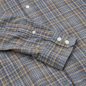 A close-up of the HARTFORD - PAUL Checked Flannel Shirt in Grey highlights the blue, brown, and grey plaid cotton fabric, with a focus on the cuff and sleeve featuring visible white buttons.