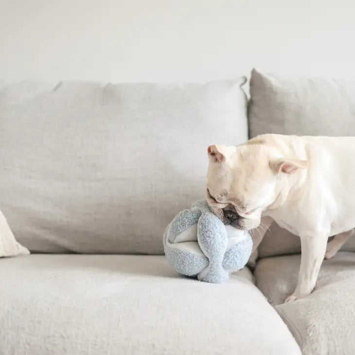 The MONTI Dog Toy in Oat by LAMBWOLF COLLECTIVE, resembling a Montessori snuffle ball with its beige-toned, plush knots and spherical shape, sits against a white background as both a modern decor piece and an engaging boredom buster.