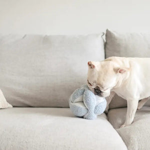 The MONTI Dog Toy in Oat by LAMBWOLF COLLECTIVE, resembling a Montessori snuffle ball with its beige-toned, plush knots and spherical shape, sits against a white background as both a modern decor piece and an engaging boredom buster.
