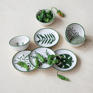 CREATIVE COOP's HAND-PAINTED STONEWARE BOWLS WITH BOTANICAL DESIGN, some holding green peppers or grains, are arranged on a light beige surface—each bowl highlights its unique handcrafted artistry.