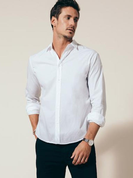 A man in the FRANK &amp; EILEEN Finbar Men's Button Up Shirt in classic white poplin stands with rolled sleeves and hands in pockets, looking to the side. He has short dark hair, wears a watch, and poses against a light background.