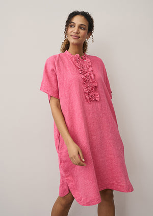A woman models the 0039 ITALY DAISY LINEN DRESS, featuring ruffled detailing along the button placket. Only her lower face and upper torso are visible as she stands against a light background, showcasing modern femininity.