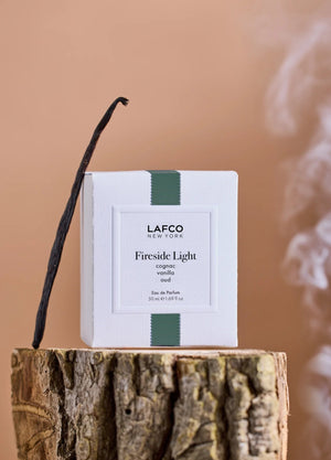 A round glass bottle of LAFCO Fine Fragrance, Fireside Light 50ml, a vegan perfume with a long-lasting scent, contains yellow liquid and is topped with a marbled green cap, displayed against a plain white background.