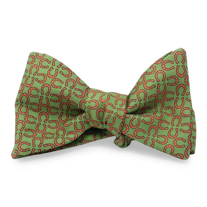 A handmade silk bow tie by Bird Dog Bay, the Peter-Blair Ringers design in green and red with a repeating circular pattern, features adjustable neck sizing and is displayed on a white background.