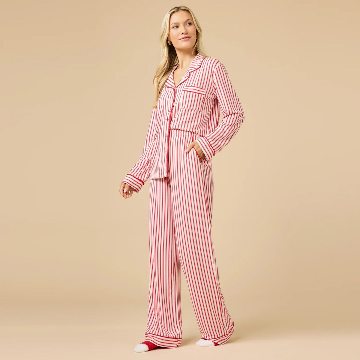 A woman wears the SOFTIES ARIA SLIM NOTCH COLLAR PJ SET, featuring a long-sleeved button-down top and matching wide-leg pants in red and white vertical stripes with red piping details.
