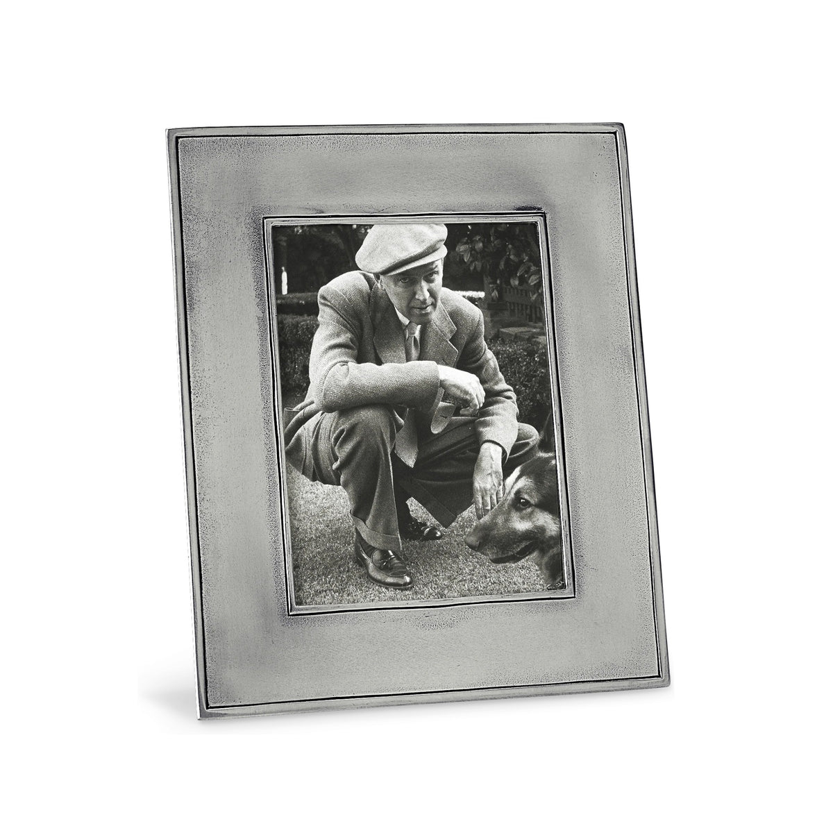A black-and-white photo in the MATCH Lombardia Rectangular Pewter Photo Frame by MATCH shows a man in a suit and flat cap crouching on grass, gesturing to a dog, with greenery, bushes, and classic wood backing in the background.