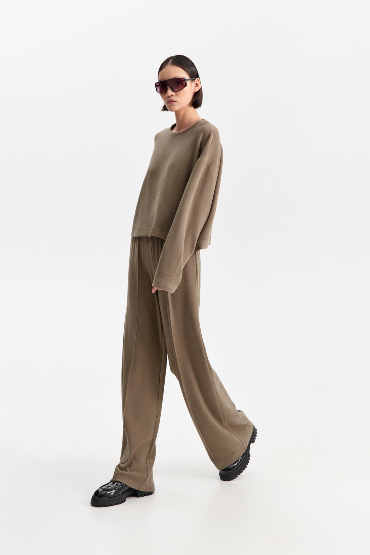 The ELEH - THE SCALA SWEATSHIRT by ELEH is a taupe, long-sleeve cropped sweatshirt featuring dropped shoulders and a relaxed fit, shown against a plain white background.