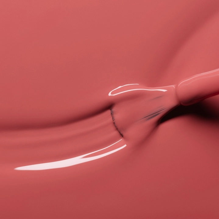 A close-up of a brush applying the smooth, glossy MANUCURIST - GREEN™ NAIL POLISH IN ROSEWOOD by MANUCURIST INC in a dusty pink rosewood shade on a flat surface, creating gentle curved lines in the polish.