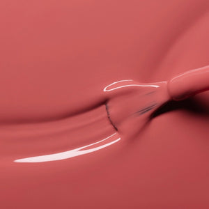 A close-up of a brush applying the smooth, glossy MANUCURIST - GREEN™ NAIL POLISH IN ROSEWOOD by MANUCURIST INC in a dusty pink rosewood shade on a flat surface, creating gentle curved lines in the polish.