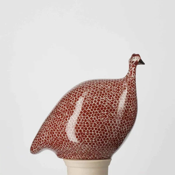The LES CERAMIQUES DE LUSSAN Medium Ceramic French Guinea in Bordeaux Spotted White, featuring a rounded body inspired by French guinea hens, is displayed on a white pedestal against a plain light background.