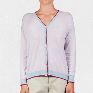 A woman wears the IN BED WITH YOU - BATWING SLEEVE CARDIGAN by IN BED WITH YOU/CLAUDIOLAI SRL, an orange V-neck with red and white trim, buttoned down the front, styled with multicolored patterned pants against a plain white background.
