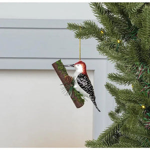 WOODPECKER ON TREE ORNAMENT featuring a glass woodpecker perched on a decorative branch with small pinecones and moss, perfect for woodland holiday decor.
