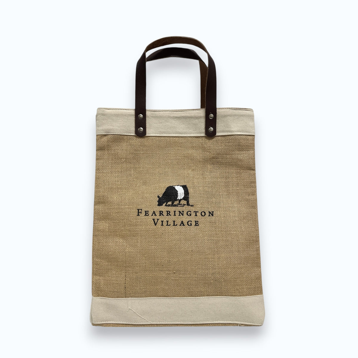 The FEARRINGTON LIFESTYLE COLLECTION - BELTIE JUTE TOTE by STRAN PROMOTIONAL SOLUTIONS is a stylish, eco-friendly tan and beige jute bag with dark leather handles and an embroidered black and white badger above "Fearrington Village.