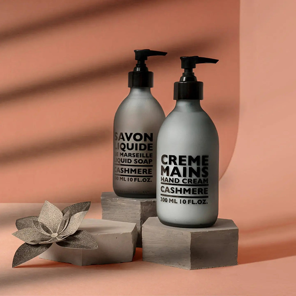 A grey bottle with a black pump, labeled &quot;CIE LUXE BRANDS COMPAGNIE DE PROVENCE CASHMERE HAND CREAM,&quot; contains shea butter and woody, spicy notes; it holds 300 ml (10 fl oz).