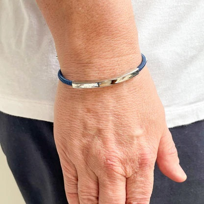 The STOLEN RICHES Algarve Bracelet features a blue nylon band, a curved silver bar, and silver end caps with an adjustable sliding clasp for a minimalist look.
