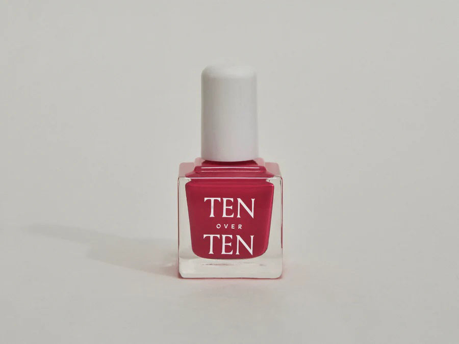 A glass bottle of TENOVERTEN - NAIL POLISH from the brand TEN OVER TEN, featuring a white cap and a dusty pink nail color. The front label displays "TEN OVER TEN" in white uppercase letters. This vegan, eight-free formula ensures both beauty and peace of mind. The background is plain and light-colored.