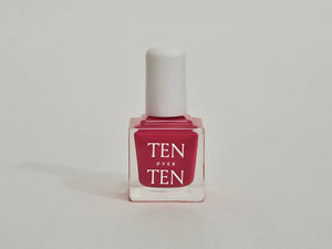 A glass bottle of TENOVERTEN - NAIL POLISH from the brand TEN OVER TEN, featuring a white cap and a dusty pink nail color. The front label displays "TEN OVER TEN" in white uppercase letters. This vegan, eight-free formula ensures both beauty and peace of mind. The background is plain and light-colored.