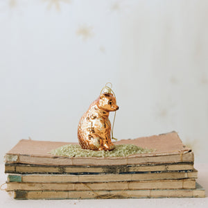A metallic gold mercury glass BEAR ORNAMENT WITH GLITTER sits on a small pile of green glitter atop a stack of old books.
