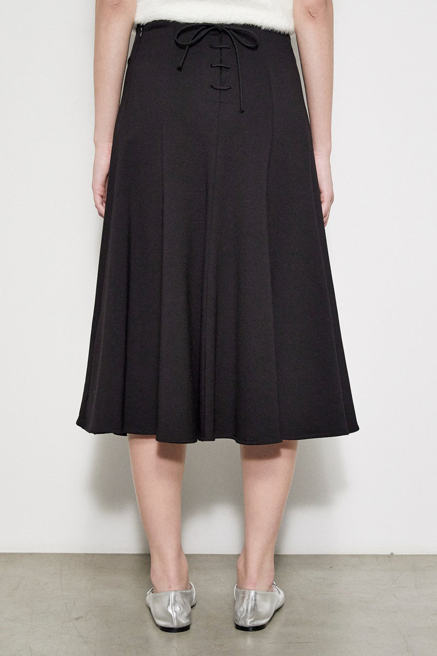 A person stands against a plain white background, displaying a side profile. They are wearing the MEIMEIJ - Swing Skirt with Lace Back, a cream-colored top featuring elegant lace detailing on the back, paired with a black knee-length A-line swing skirt and metallic silver flat shoes. The photo captures the outfit from the shoulders down to the feet.