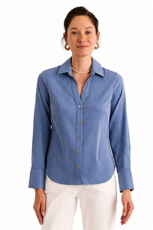 A woman stands against a plain, light background, exuding effortless style and breathable comfort in the HINSON WU Lindsey Long Sleeve Ribbon Stripe Shirt in Blue and White—a lightweight pinstripe button-up featuring gold buttons—paired with white pants.