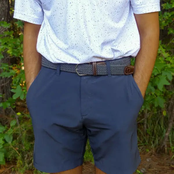 The ROOSTAS - SCOTTSDALE WOVEN STRETCH BELT by ROOSTAS is a stylish grey braided stretch belt with brown leather accents, white stitching, and a silver buckle—perfect for golf or casual wear, shown coiled on a white background.
