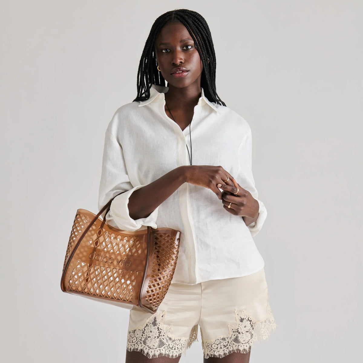 The DOLCE VITA - TOP HANDLE WHISKEY JELLY HANDBAG features a brown lattice design, curved handles, and “dolce vita” embossed on the front—a stylish, see-through tote perfect for vacations.