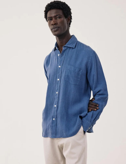 A person with short, curly black hair is seen from behind wearing the HARTFORD - PAUL Linen Shirt in Denim by HARTFORD, set against a plain light background.