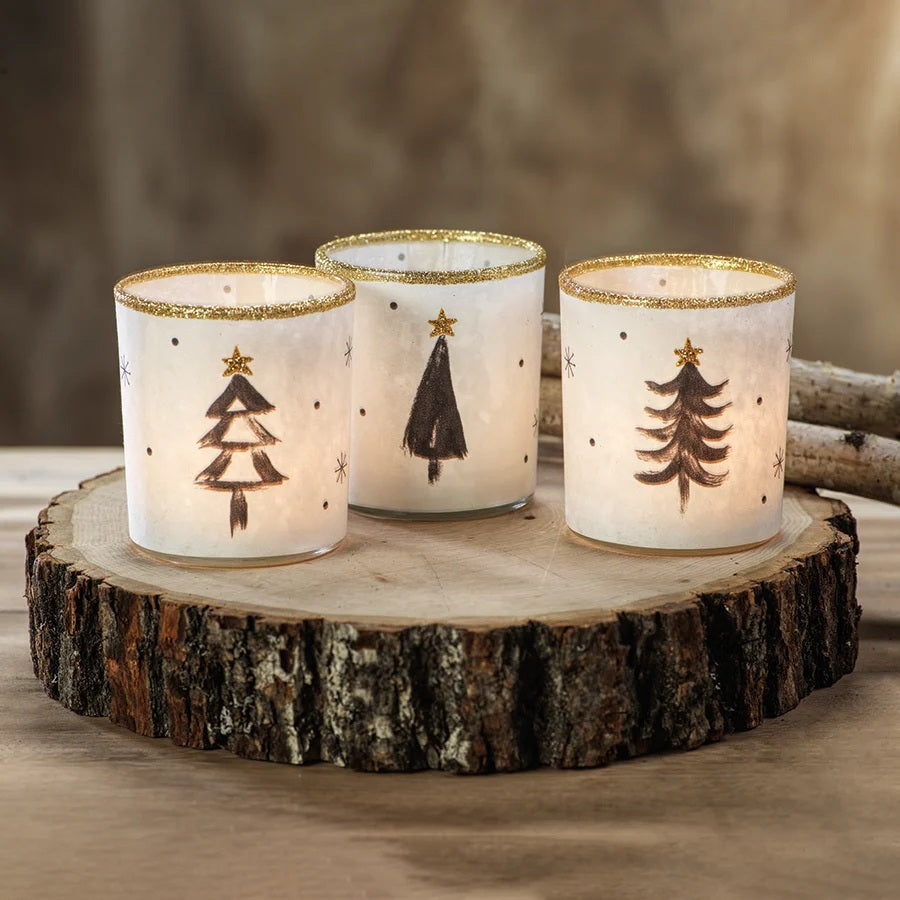 Three Zodax TREE TEALIGHT HOLDER cylindrical glass candle holders, sold individually, decorated with hand-painted black pine trees, gold glitter stars, and gold rims in an assorted style.