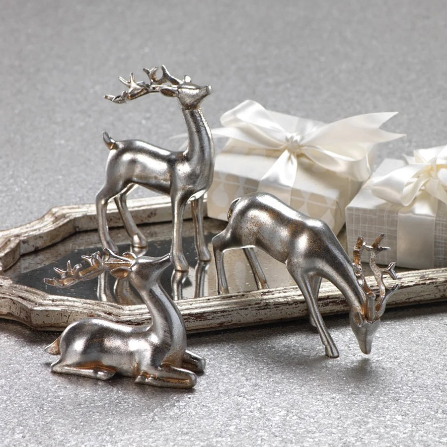Three silver-colored ZODAX DECORATIVE SILVER REINDEER polyresin figurines in assorted styles on a mirrored tray with two gift boxes wrapped in white ribbon.