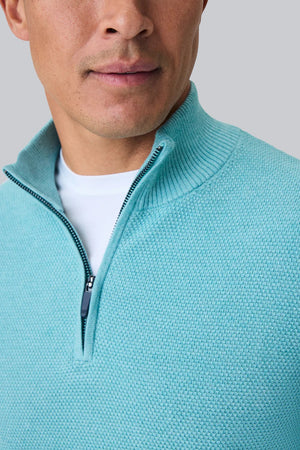 A man faces away from the camera, wearing the MACK WELDON Tech Linen Quarter Zip in Deep Lagoon Heather with COOLMAX® technology and gray pants. The background is plain light gray.