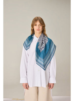 A detailed illustration of a cat and an owl sitting side by side on a branch, bordered by an intricate blue and white pattern, evokes the fine craftsmanship of the INOUI EDITIONS - CHOUETTE SQUARE SCARF IN BLUE by INOUI.