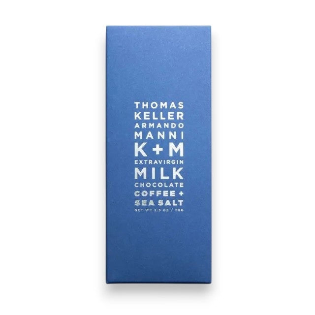 A blue package of K &amp; M EXTRAVIRGIN CHOCOLATE, labeled “K+M - EXTRAVIRGIN MILK CHOCOLATE, COFFEE AND SEA SALT BAR” in centered white text, featuring a rich blend of roasted coffee bean and sea salt flavors.