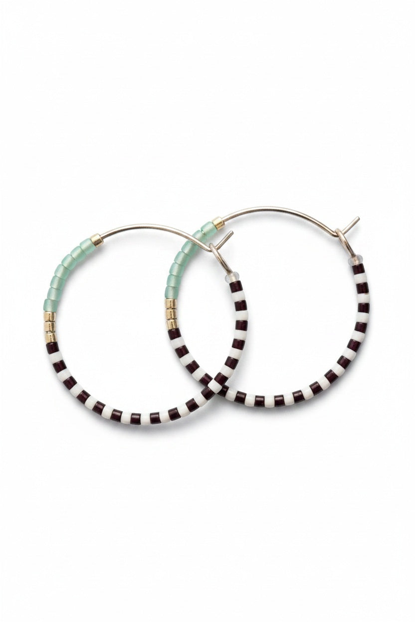 The ALICE RISE MIDI COLORLOOP EARRINGS IN SERRATA feature 14k gold filled hoops with alternating black and white beads, light blue Japanese glass beads, and gold accents—an ideal handmade jewelry piece from ALICE RISE.