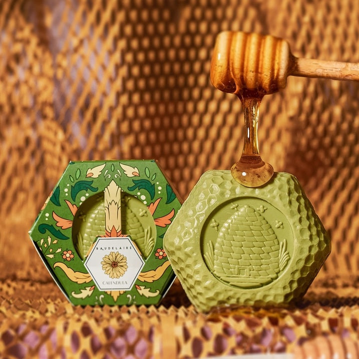 Hexagonal box of BAUDELAIRE - CALENDULA HONEY SOAP 3.5 OZ, featuring green floral packaging with a central clear window displaying the triple-milled moisturizing bar and a floral design label on top, by BAUDELAIRE.