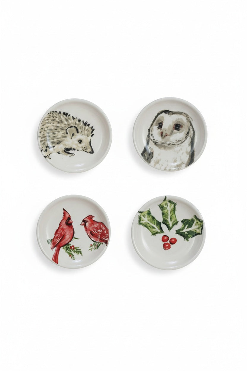 Six small, round Creative Coop stoneware dishes with hand-painted botanical animal illustrations of a hedgehog, owl, birds, or winter greenery.