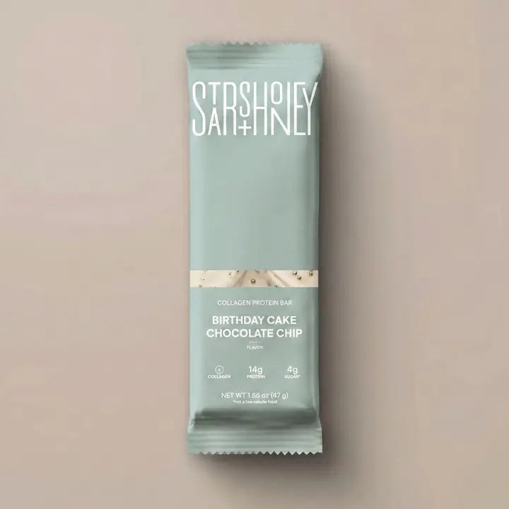 A STARS+HONEY-BIRTHDAY CAKE CHOCOLATE CHIP protein bar by STARS+HONEY, with natural sprinkles and notes of vanilla yellowcake, is wrapped in light blue packaging and displayed against a plain beige background.