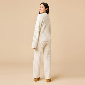 A woman wearing the SOFTIES CABLE KNIT MARSHMALLOW V-NECK WITH FLARED SLEEVE AND PANT SET, a marshmallow-soft, cream-colored cable knit v-neck sweater with wide sleeves and matching lounge pants.