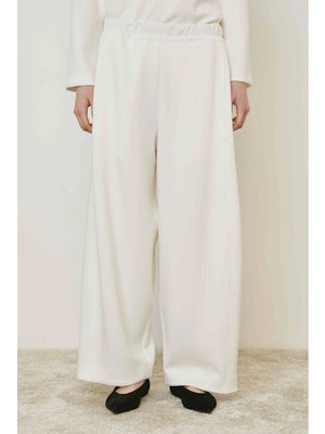 A person wears MEIMEIJ - PULL ON PANTS, featuring a wide-leg silhouette and elastic waistband, standing on a beige carpet in black shoes. These chic MEIMEIJ pants are made in Italy; the upper body is mostly out of frame.